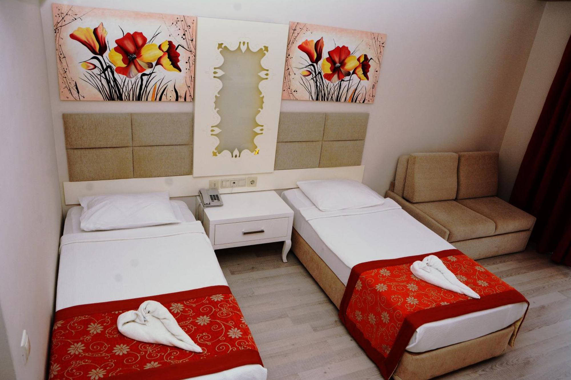 Miramor Hotel & Spa Antalya Luaran gambar The photo shows a hotel room featuring two single beds with white linens, each adorned with a decorative red throw. The headboards are upholstered in a light beige fabric. Above the beds, there are two large artwork pieces depicting colorful flowers.