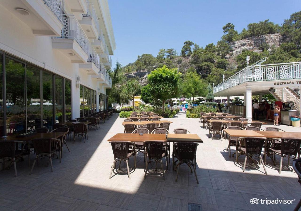 Miramor Hotel & Spa Antalya Luaran gambar The photo shows an outdoor dining area, likely at a restaurant or cafe. There are several tables with chairs arranged neatly on the paved ground, and some greenery, such as trees and plants, is visible in the background. The setting appears bright an