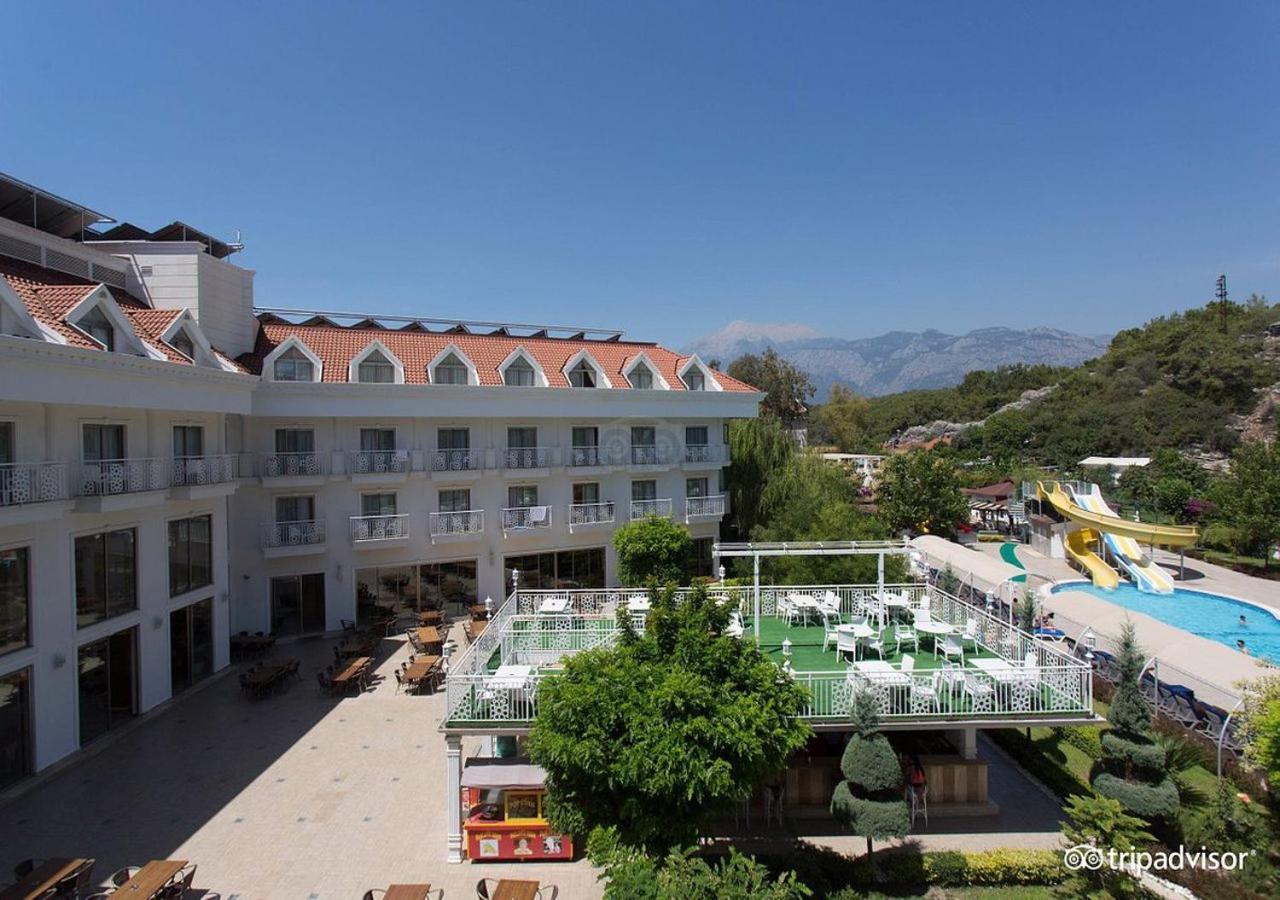 Miramor Hotel & Spa Antalya Luaran gambar The photo shows a hotel or resort facility with a well-maintained exterior. There is a large green area with grass and some trees, likely intended for relaxation or recreational activities. In the background, there are water slides suggesting an amus